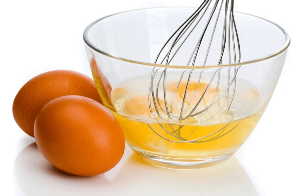 Whisking eggs in a glass bowl to prepare a healthy vegetable omelette base.