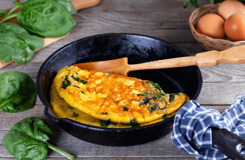 Cooking a healthy vegetable omelette with spinach in a cast-iron skillet.