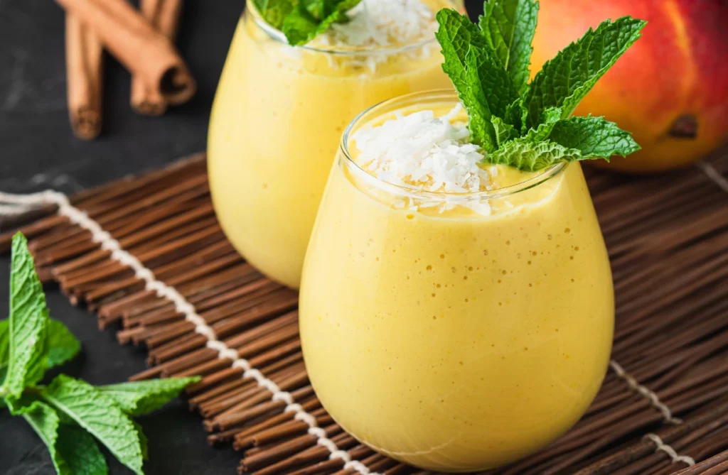 A refreshing mango lassi garnished with cardamom and a slice of fresh mango.