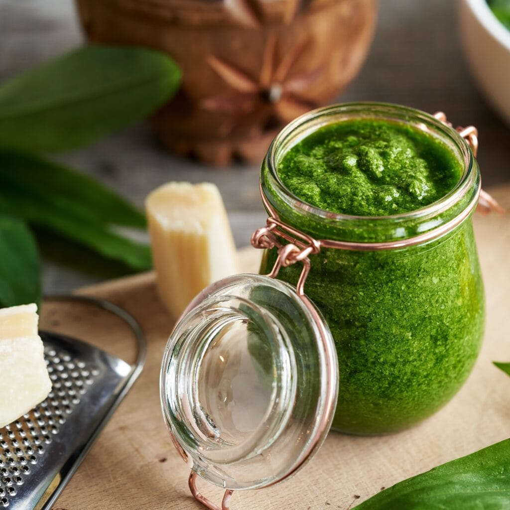 Ingredients for creamy pesto chicken skillet laid out on a counter, including chicken breasts, pesto sauce, and fresh herbs.